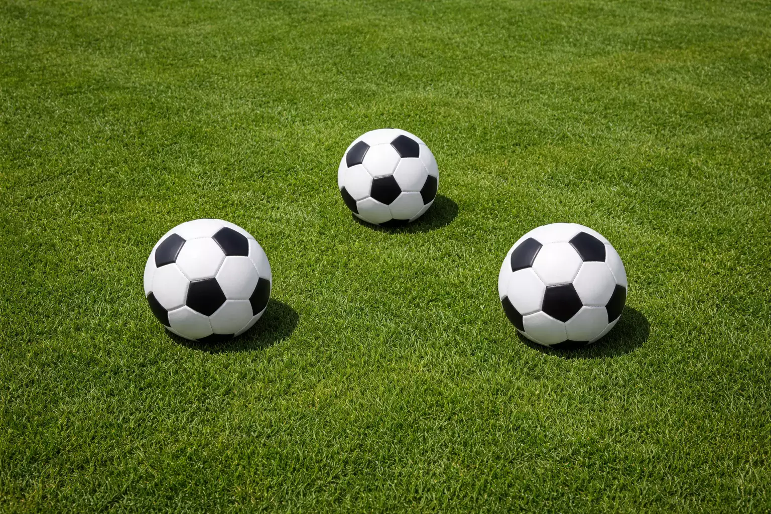 Tre palloni da calcio disposti in triangolo su prato verde